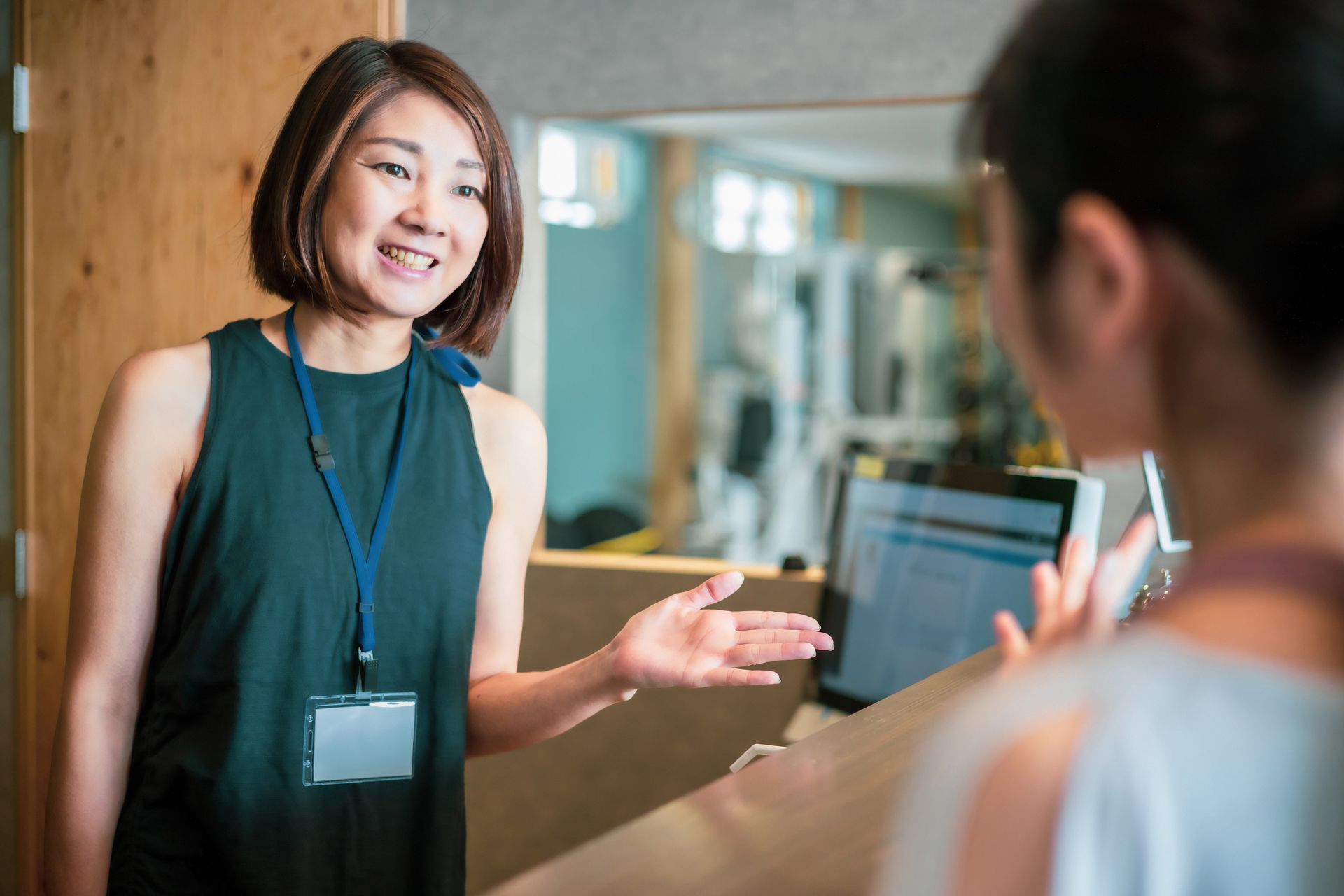 Two people talking in a bright office, one smiling and gesturing with a badge on a lanyard.