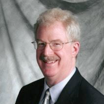 Portrait of a smiling man in a suit and glasses against a gray backdrop