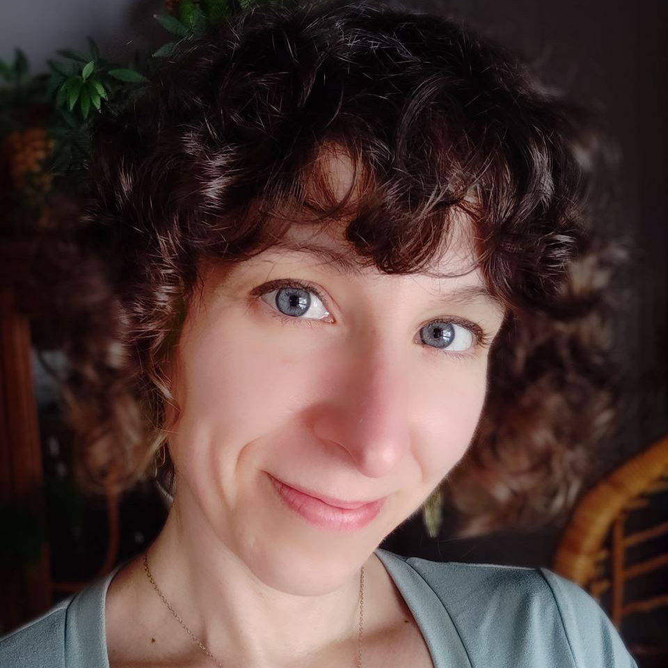 Close-up portrait of a smiling person with curly dark hair and blue eyes indoors