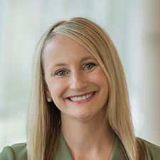 Smiling blonde woman in a green top against a softly lit indoor background