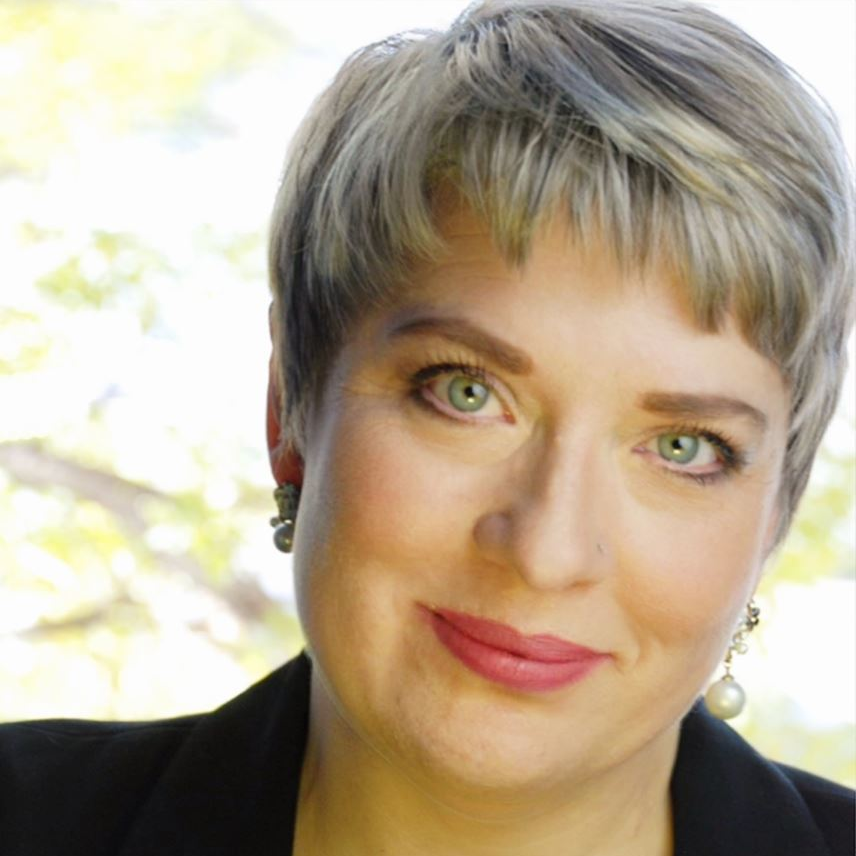 Close-up portrait of a woman with short gray hair and green eyes, softly smiling outdoors.