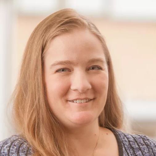 Close-up portrait of a smiling person with long light brown hair against a softly blurred background