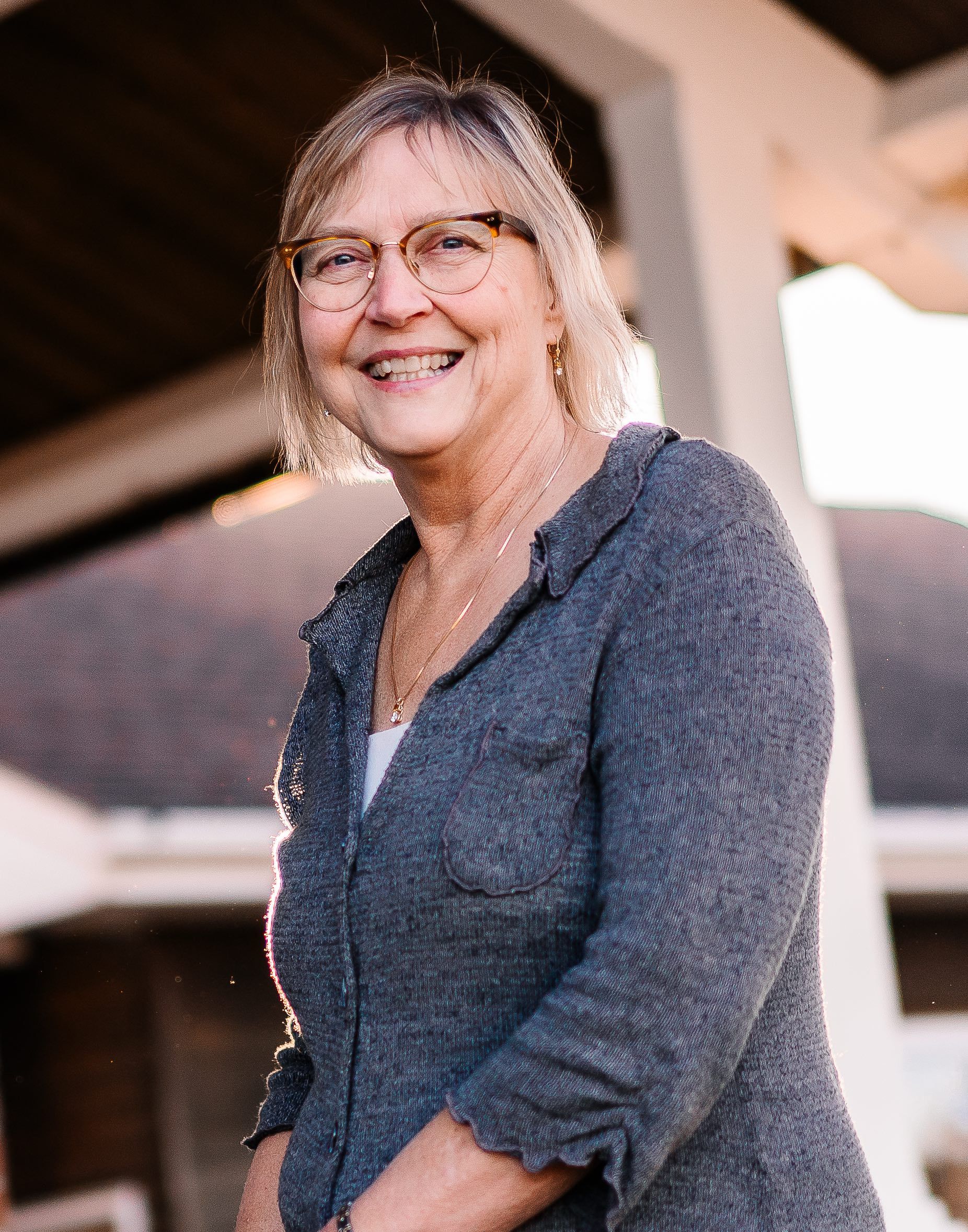 Portrait of a smiling person with glasses and dark hair against a light background
