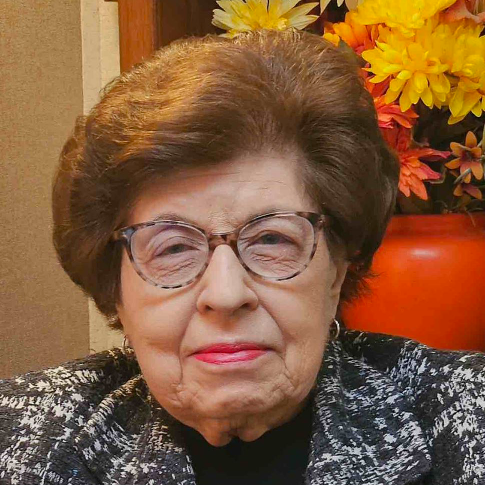 Portrait of a smiling woman with curly hair wearing a gray blazer and red lipstick