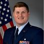 Official portrait of a uniformed man with an American flag backdrop, smiling at the camera