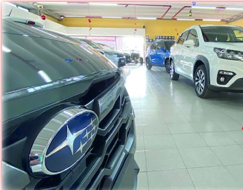 Autosalone con una Subaru nera in primo piano, un SUV bianco sulla destra e auto blu sullo sfondo.