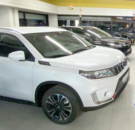Un SUV bianco è esposto in uno showroom, con altre auto allineate alle sue spalle.