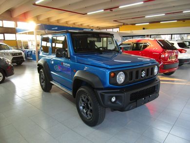 SUV fuoristrada blu in uno showroom con auto rosse sullo sfondo.
