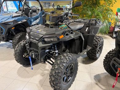 Un quad nero parcheggiato all'aperto, con altri veicoli fuoristrada e piante sullo sfondo.
