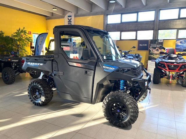 Un quad nero parcheggiato all'aperto, con altri veicoli fuoristrada e piante sullo sfondo.
