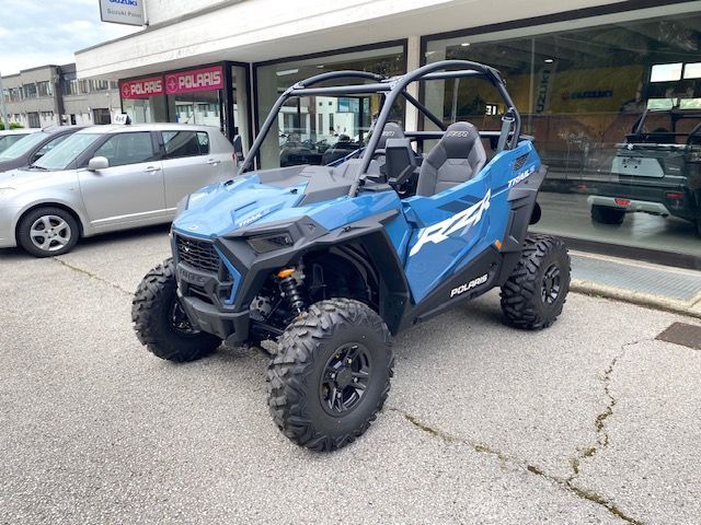 Un quad verde fuoristrada parcheggiato davanti a un negozio, con grandi pneumatici tassellati e una borsa portaoggetti posteriore.