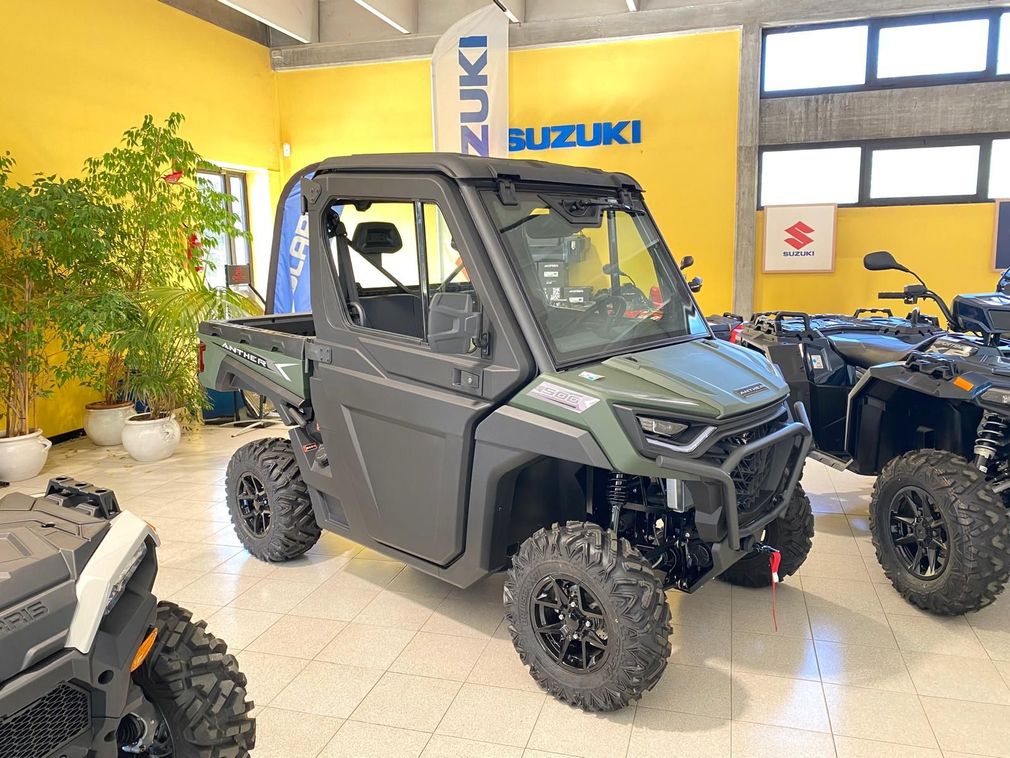 Un UTV fuoristrada grigio in una concessionaria Suzuki, con cerchi neri e pareti gialle sullo sfondo.
