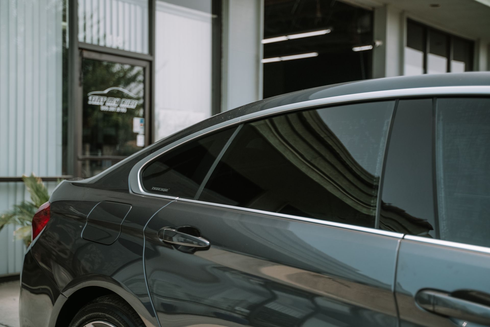Gray car with tinted windows parked in front of a building with a glass door.