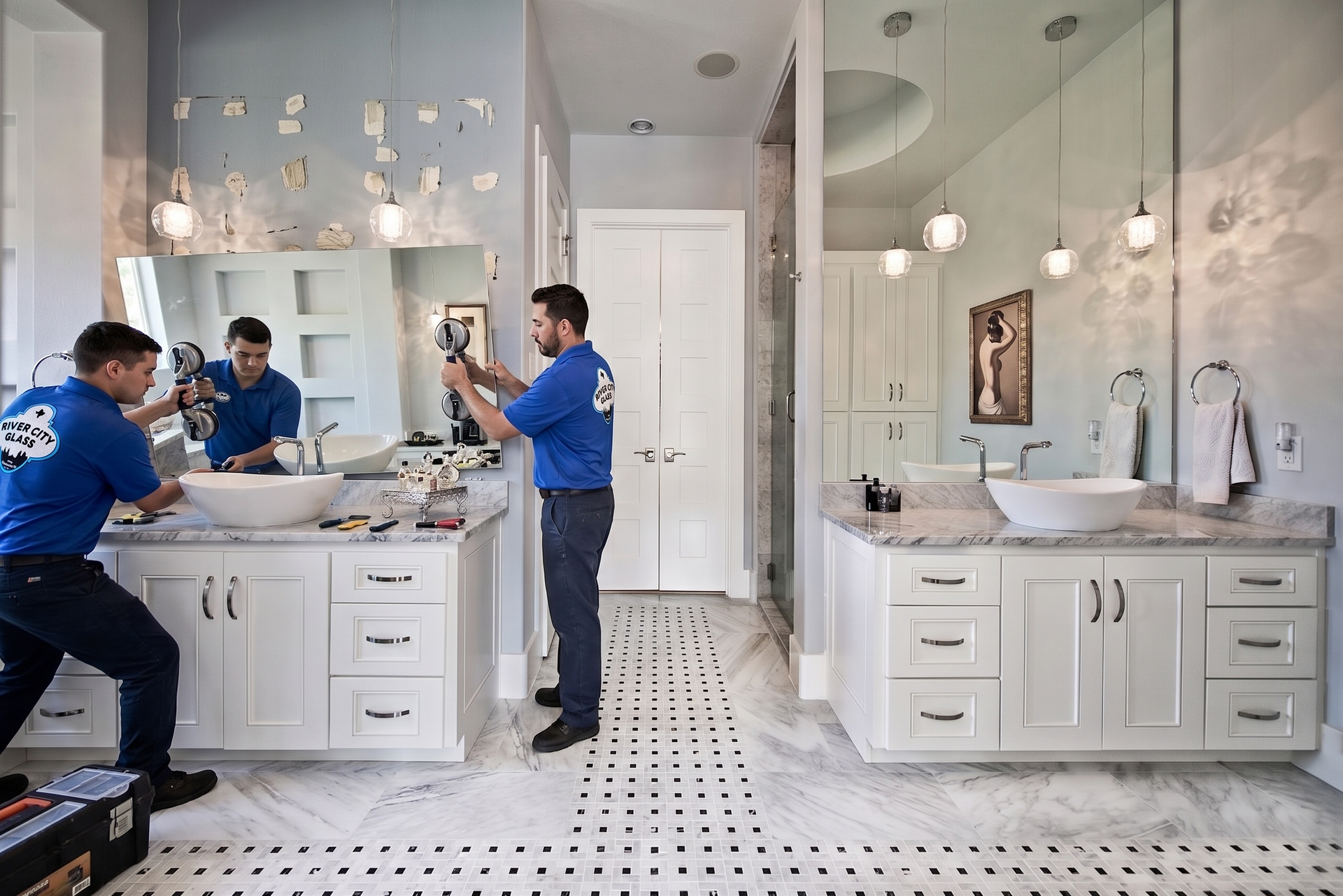 Two glaziers in blue uniforms removing vanity mirror in a bright white bathroom with double sinks and a tiled floor