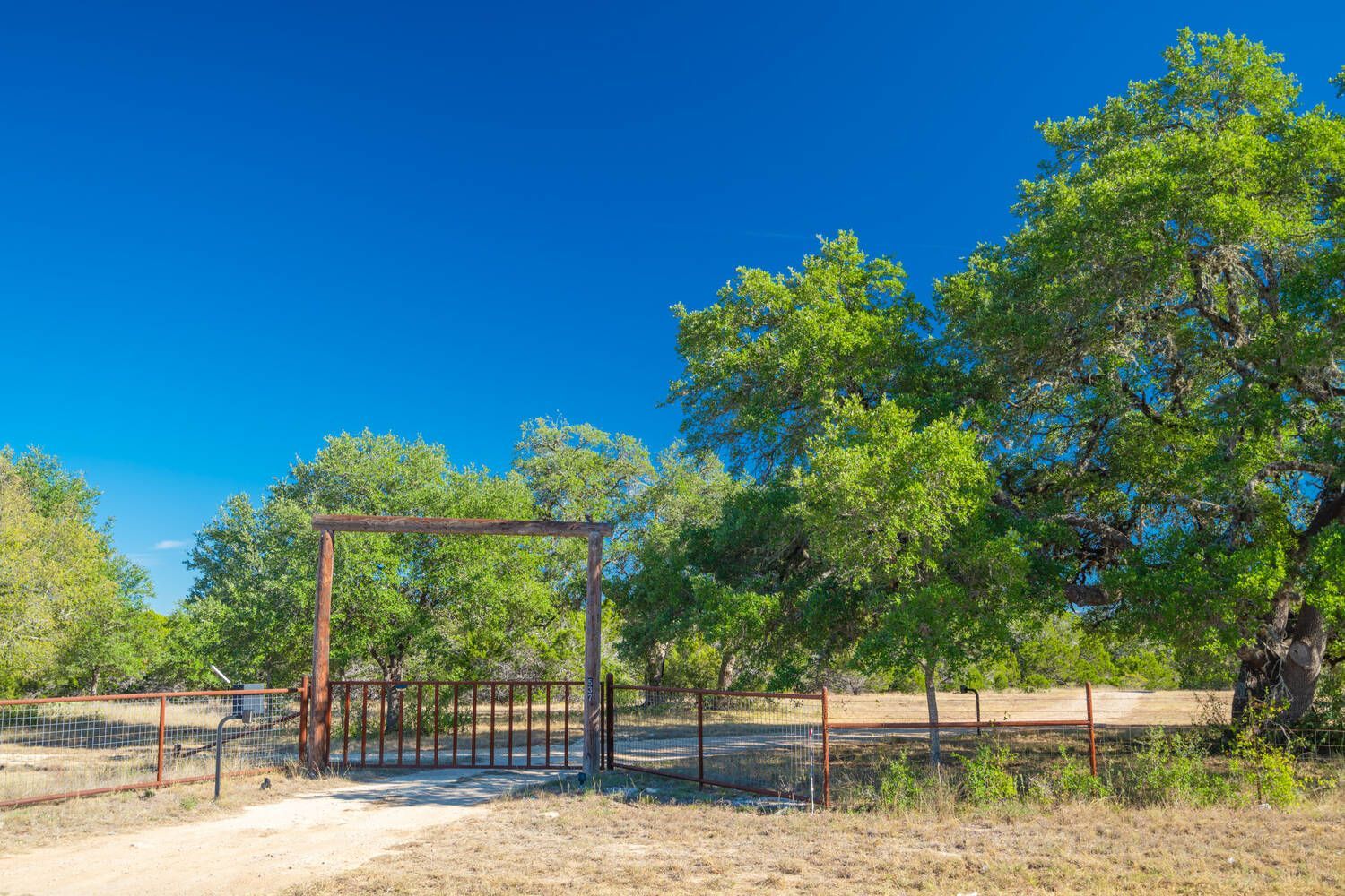 There is a gate in the middle of a field with trees in the background.