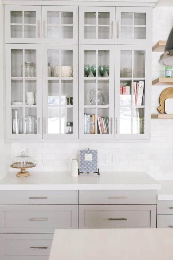 A kitchen with white cabinets , white counter tops , and glass doors.