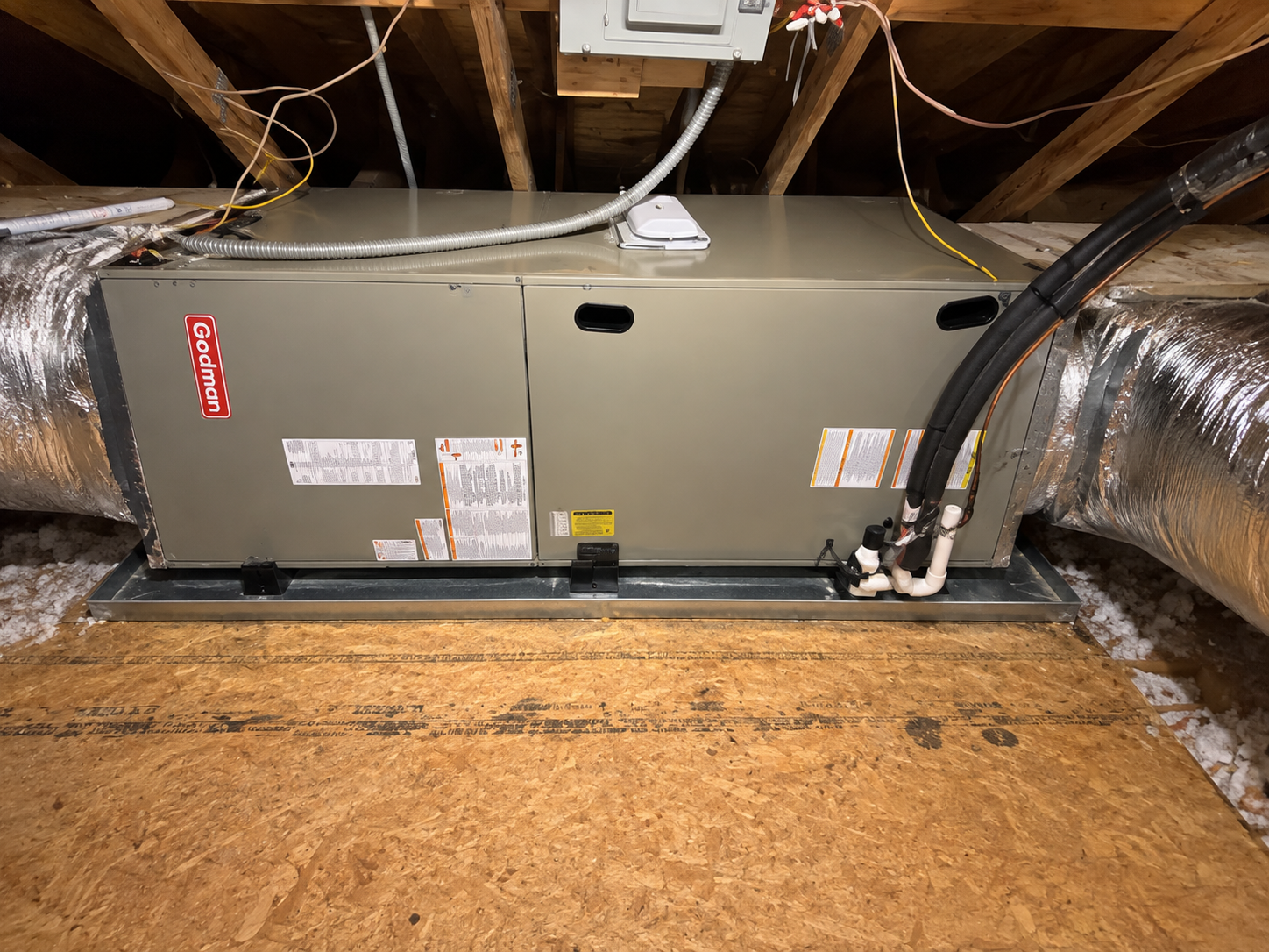 Attic HVAC unit with insulated ducts and exposed wiring above plywood flooring