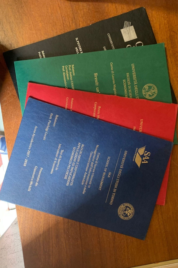 Tre passaporti impilati su un tavolo di legno: nero, verde e blu con una copertina rossa sotto.
