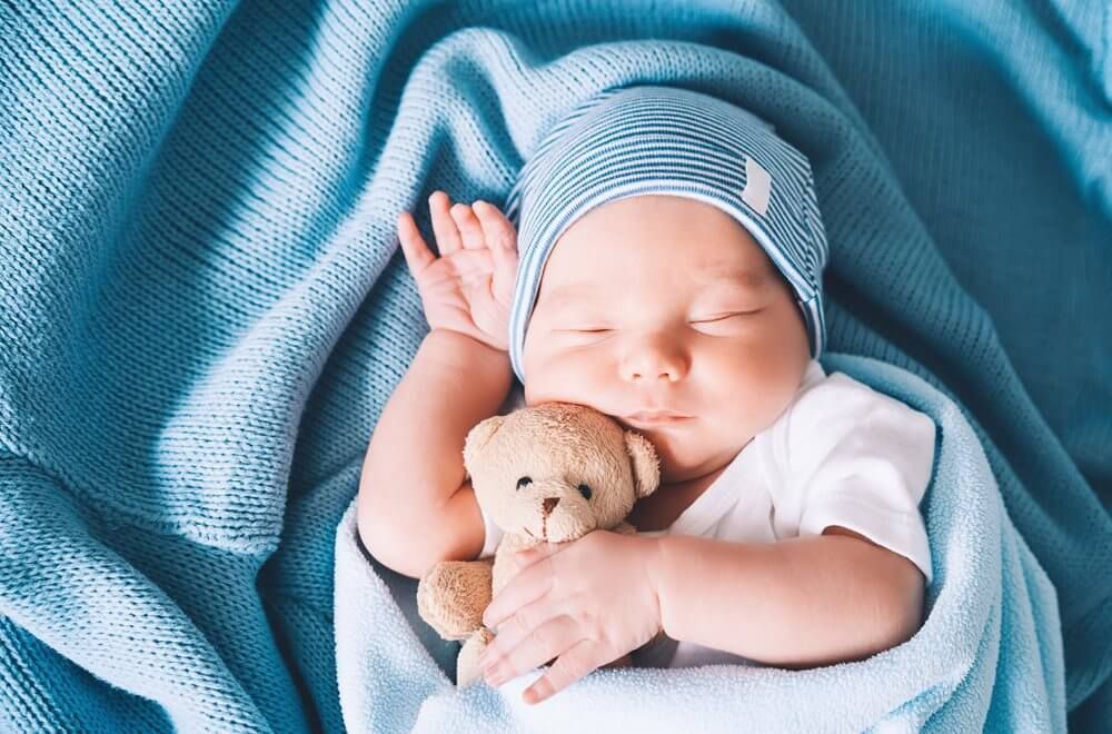 Sleeping baby wrapped in a blue blanket, holding a small teddy bear
