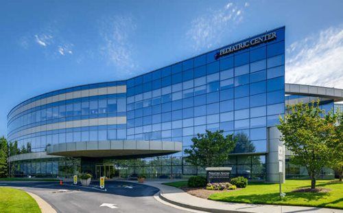 Modern Pediatric Center building with glass facade, blue sky, and green landscaping.