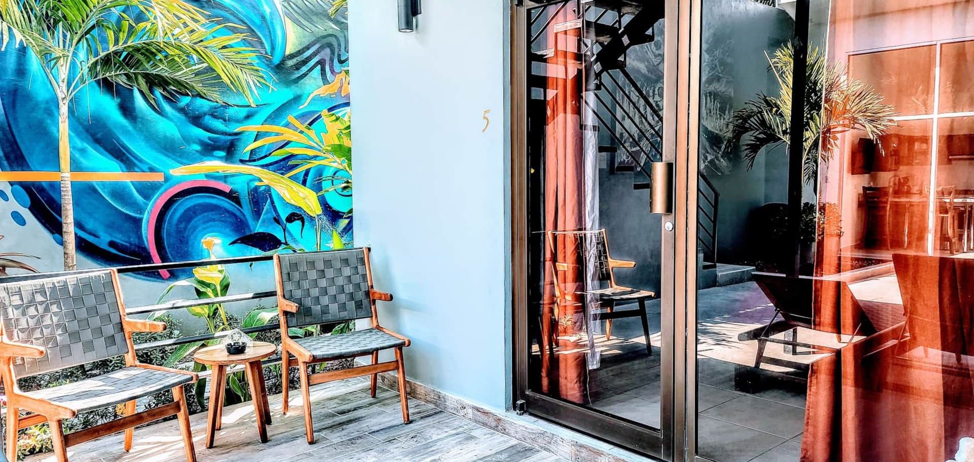 A patio with chairs , tables and a painting on the wall.