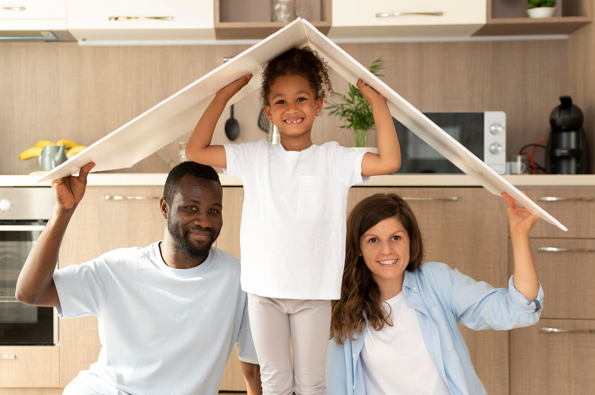 Family of three, holding a white board above their heads to form a roof in a kitchen.