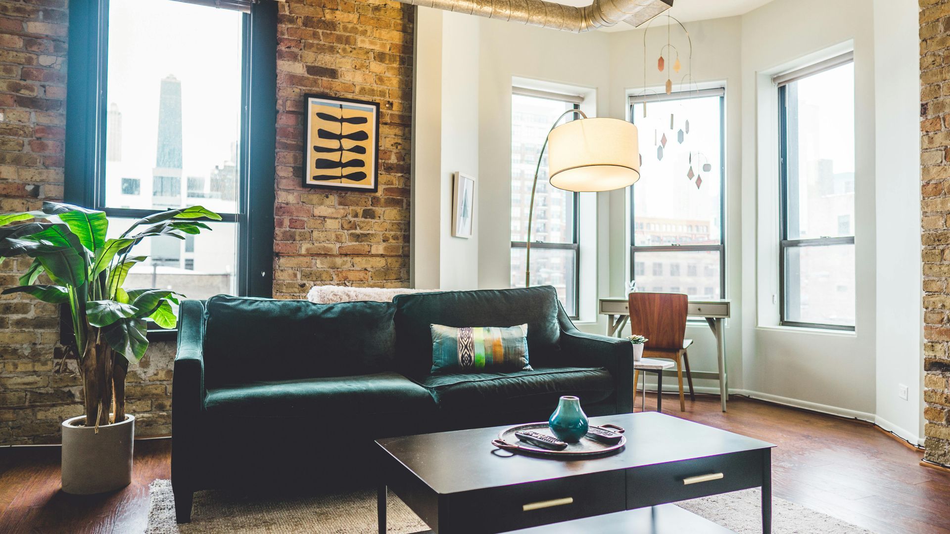 Living room with green sofa, brick wall, large windows, and a coffee table.