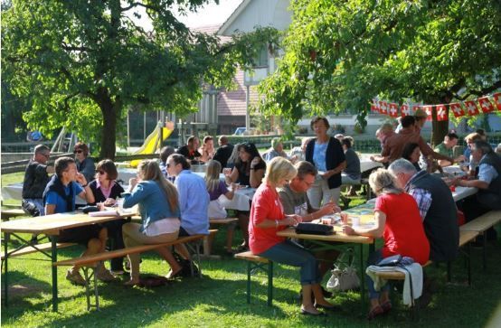 Eine Gruppe von Menschen sitzt an Picknicktischen in einem Park