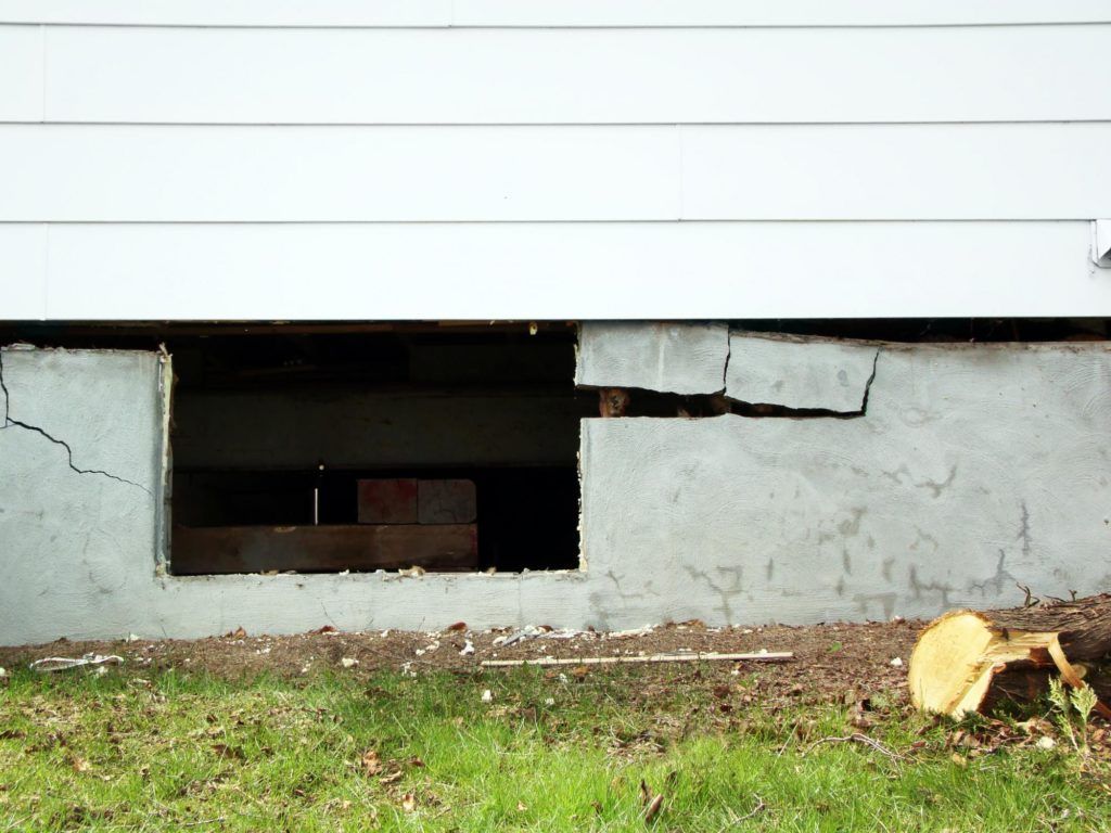 A cracked foundation of a house with a hole in it