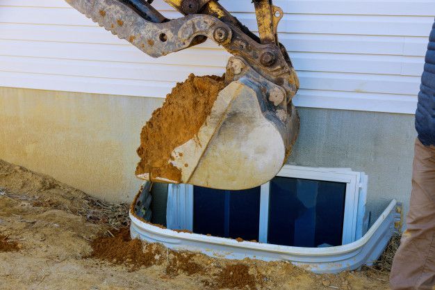 A man is using a bulldozer to dig a window well.