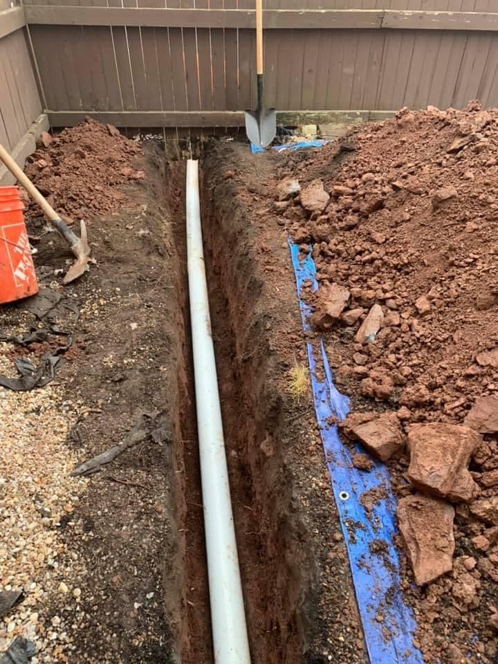 A pipe is being installed in a trench next to a pile of dirt.