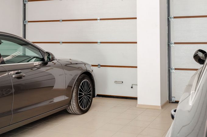 Two cars parked inside a clean garage with white doors and beige tile flooring