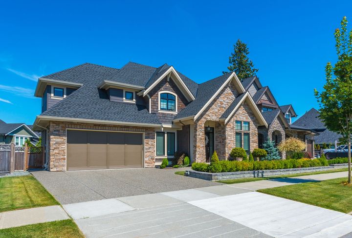 Suburban two-story brick house with a three-car garage and manicured lawn on a sunny day