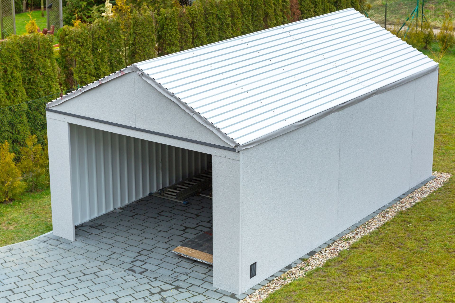 White metal garden shed with open front and pitched roof on a paved yard