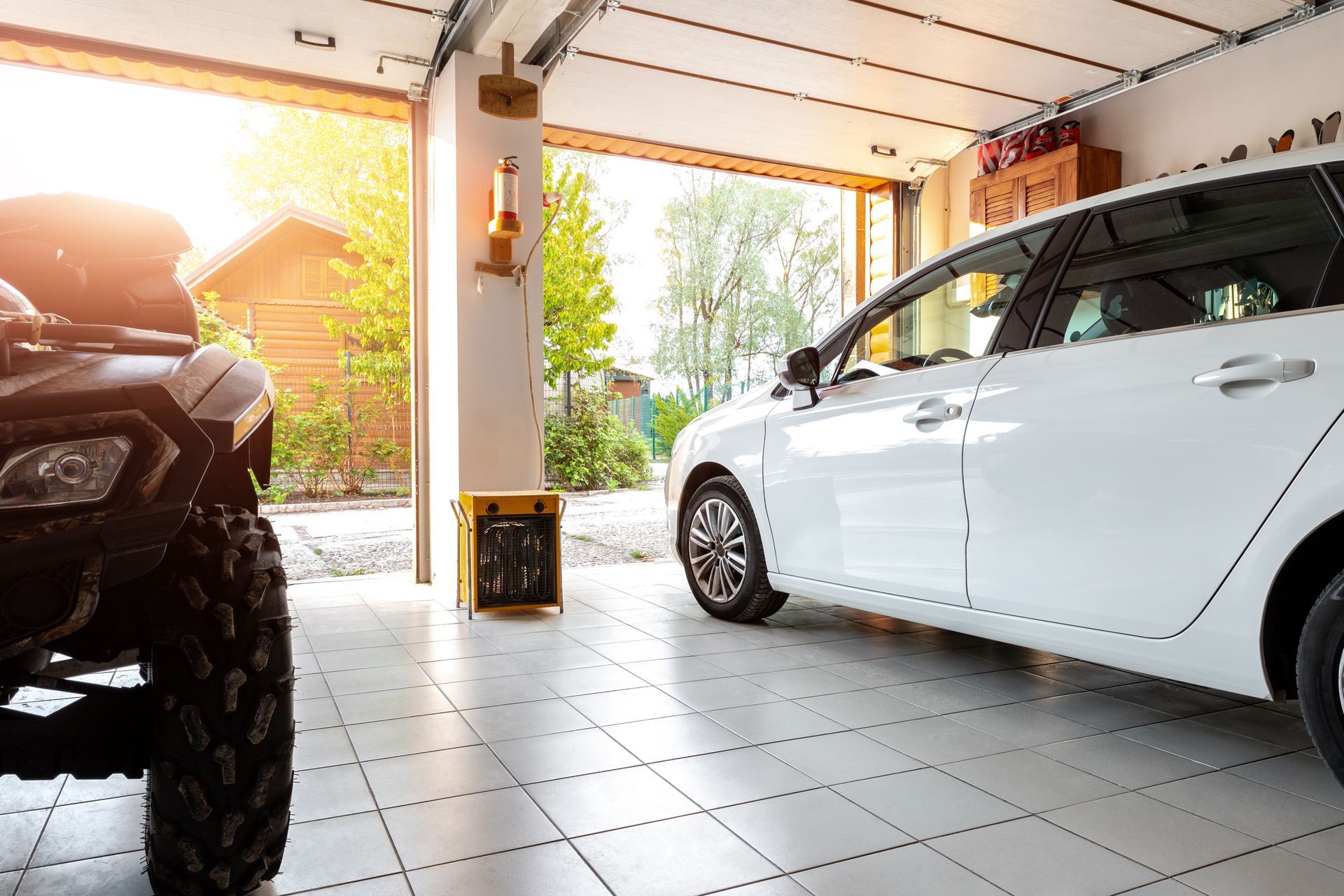 Two cars parked inside a tiled garage, with sunlight streaming in from the open door.