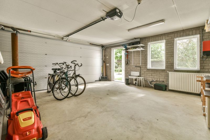 Empty garage with bicycles, orange lawnmower, and large windows letting in daylight