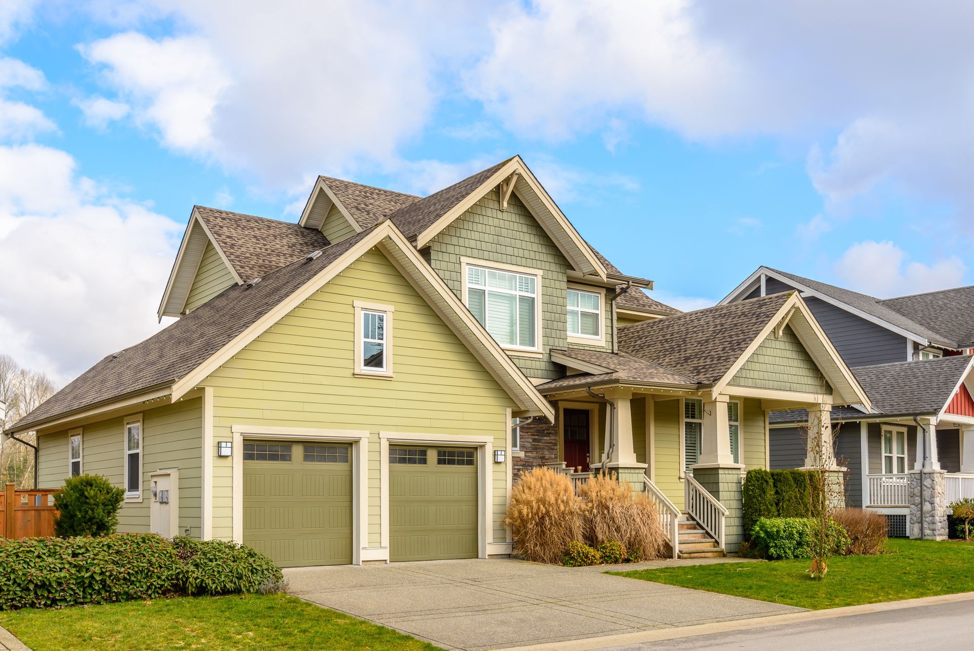Suburban beige house with a two-car garage and small front porch under a blue sky