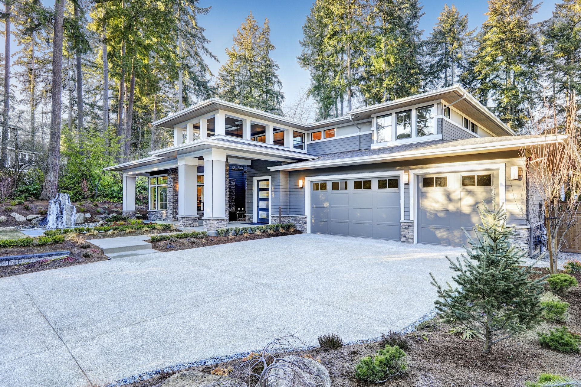 Modern two-story house with a three-car garage and wide driveway in a wooded setting