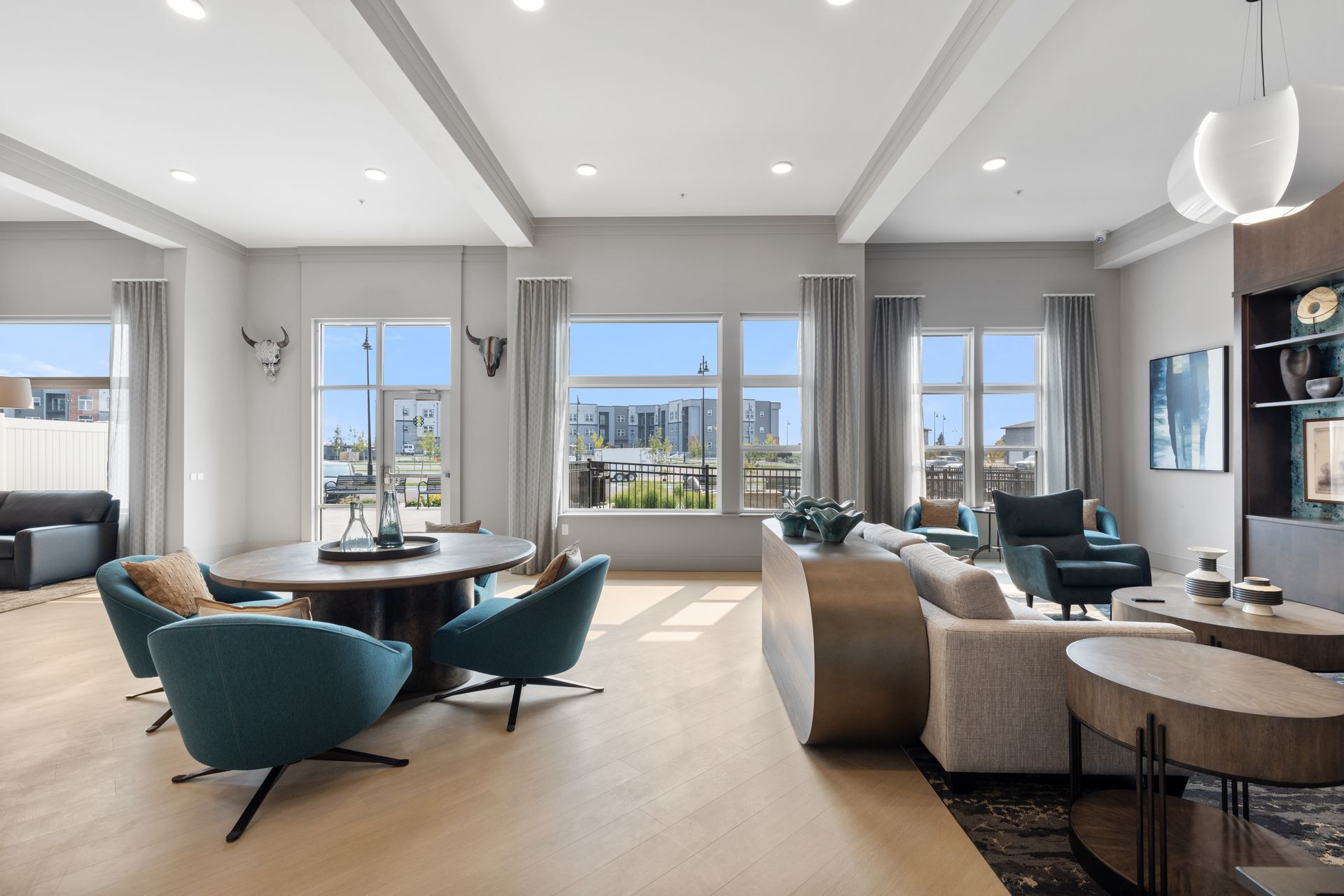 Modern living room with teal chairs, beige sofa, and large windows overlooking a city skyline