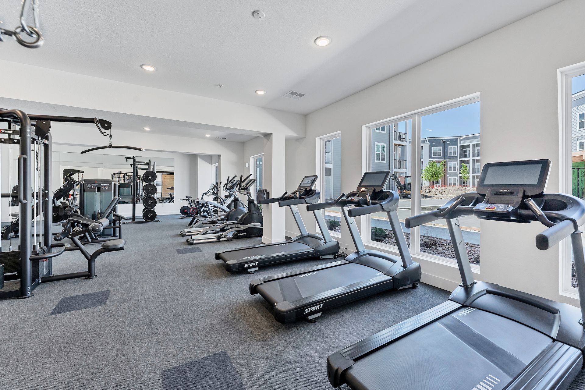Bright modern gym with treadmills, weight machines, and large windows overlooking buildings