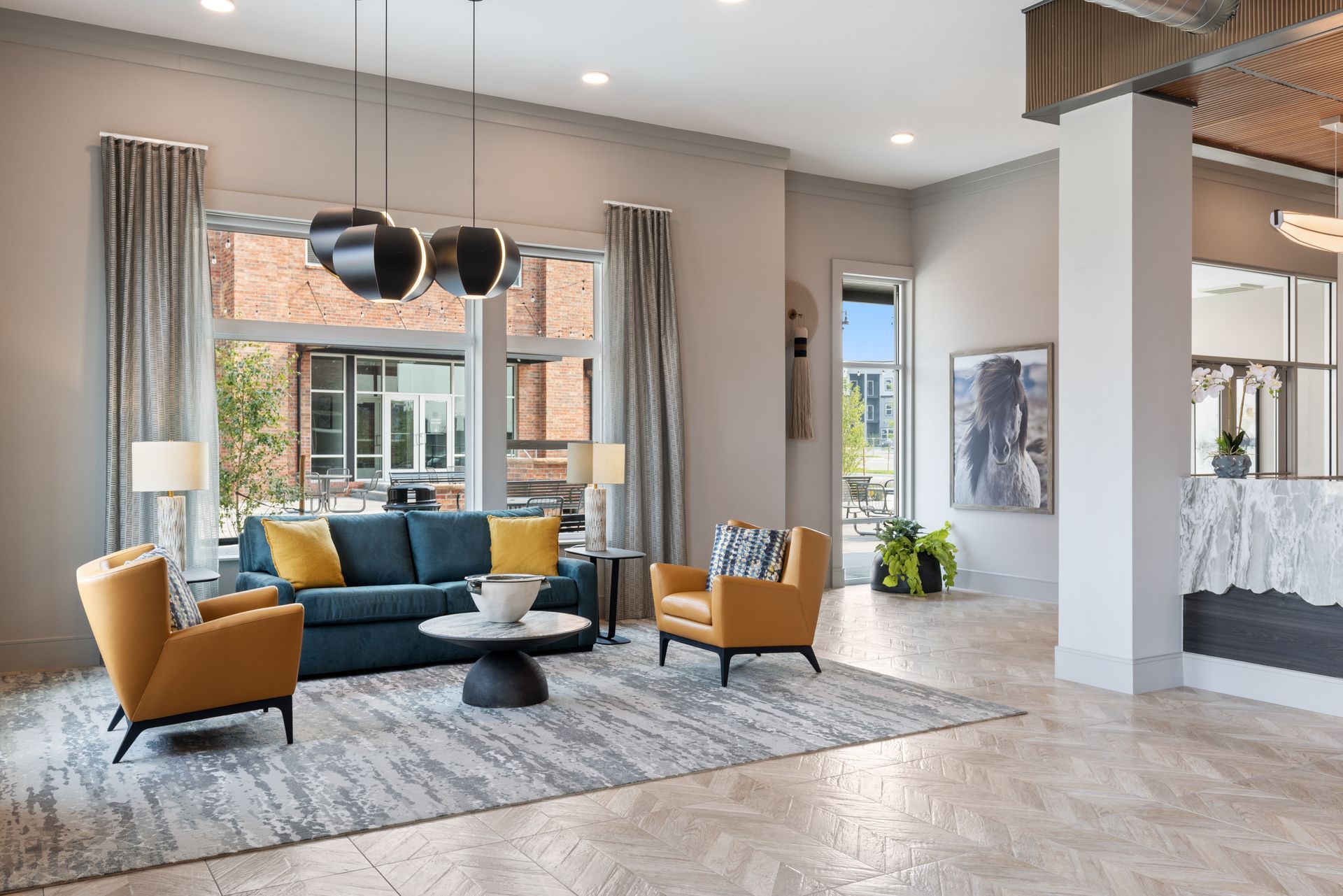 Bright modern living room with teal sofa, mustard chairs, large windows, and patterned rug