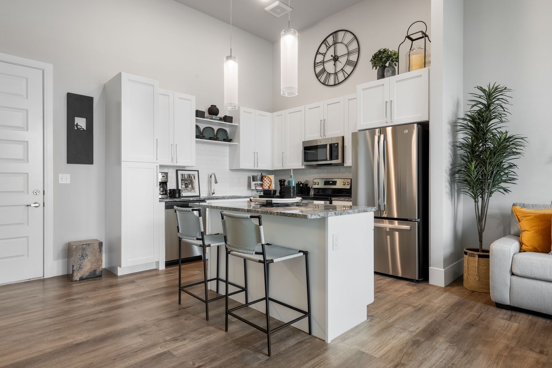 Bright modern kitchen and living area with white cabinets, stainless fridge, island stools, and hardwood floors