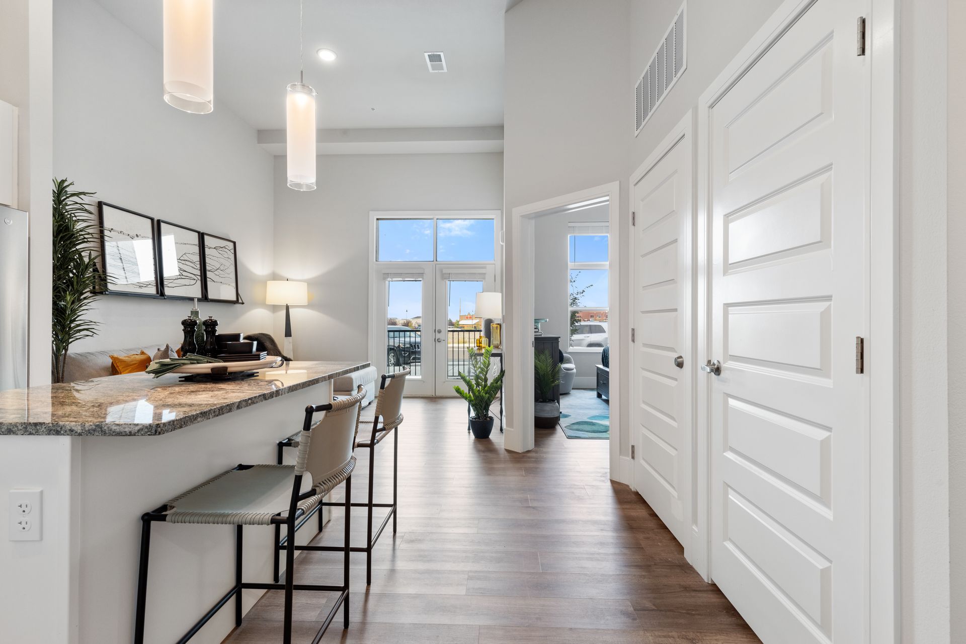 Bright modern kitchen with island, stools, white cabinets, pendant lights, and a view to a balcony.