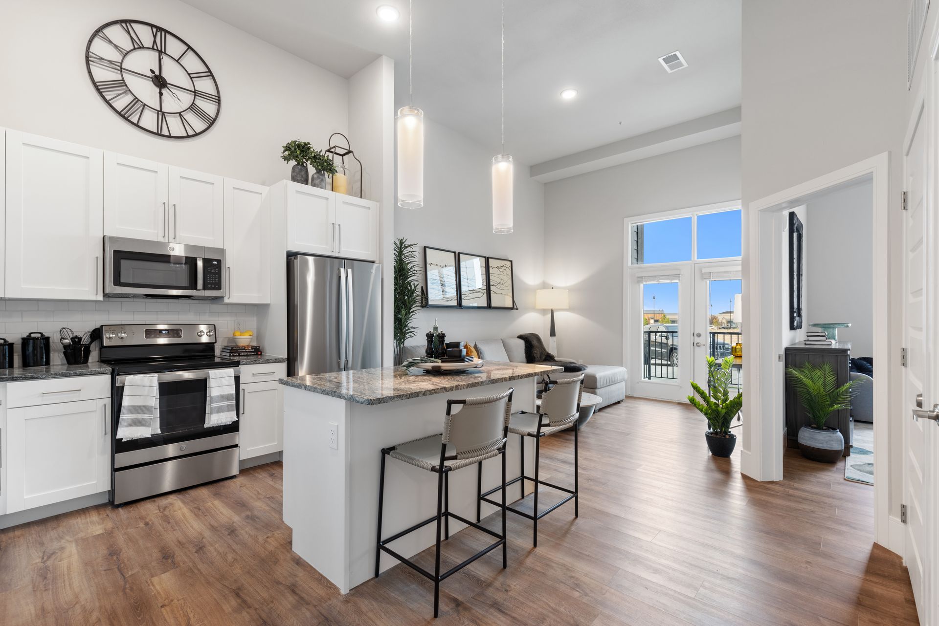 Bright modern kitchen and living area with white cabinets, stainless appliances, island, and large windows