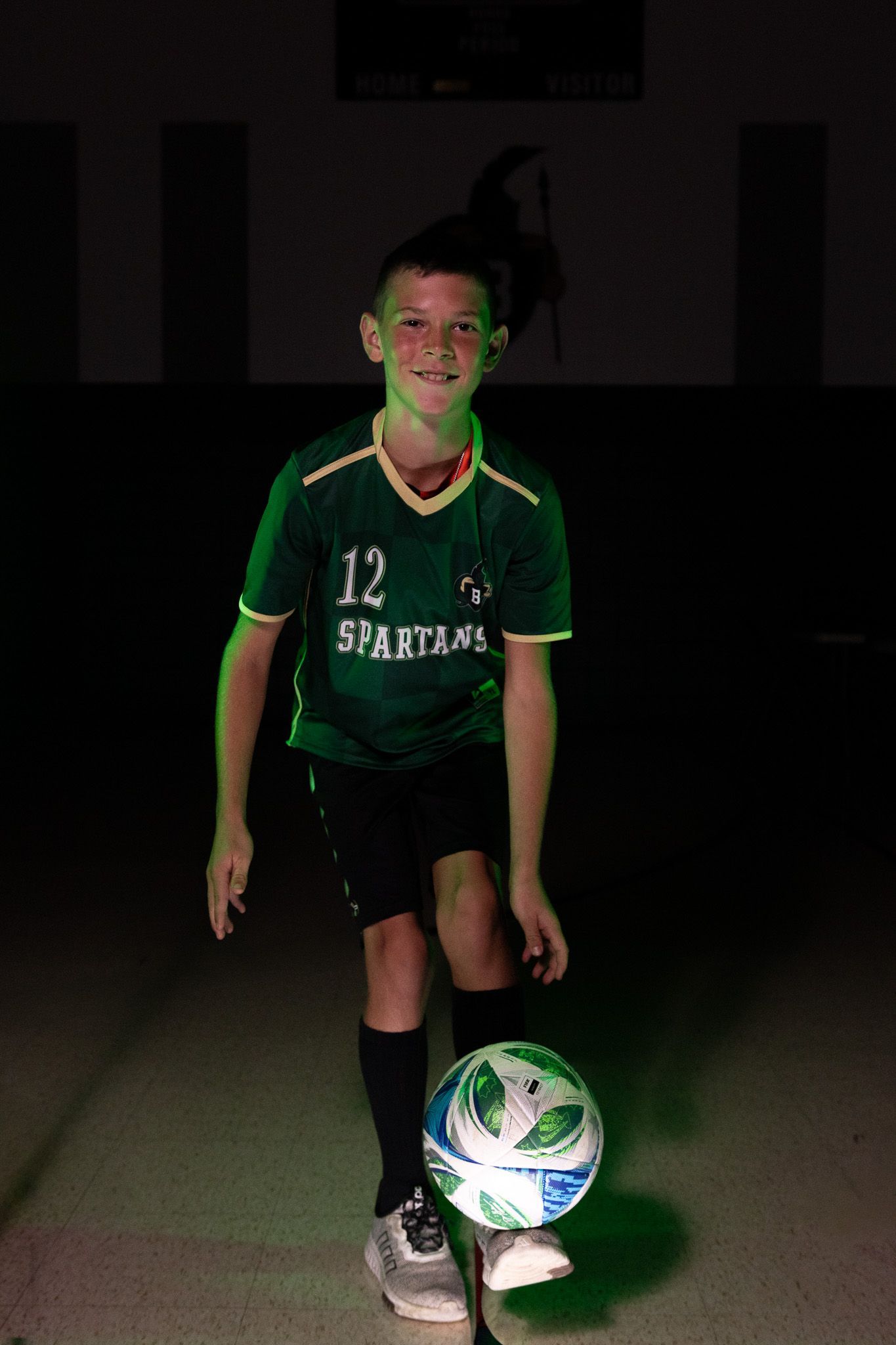 Smiling student in a green Spartans soccer jersey balancing a soccer ball