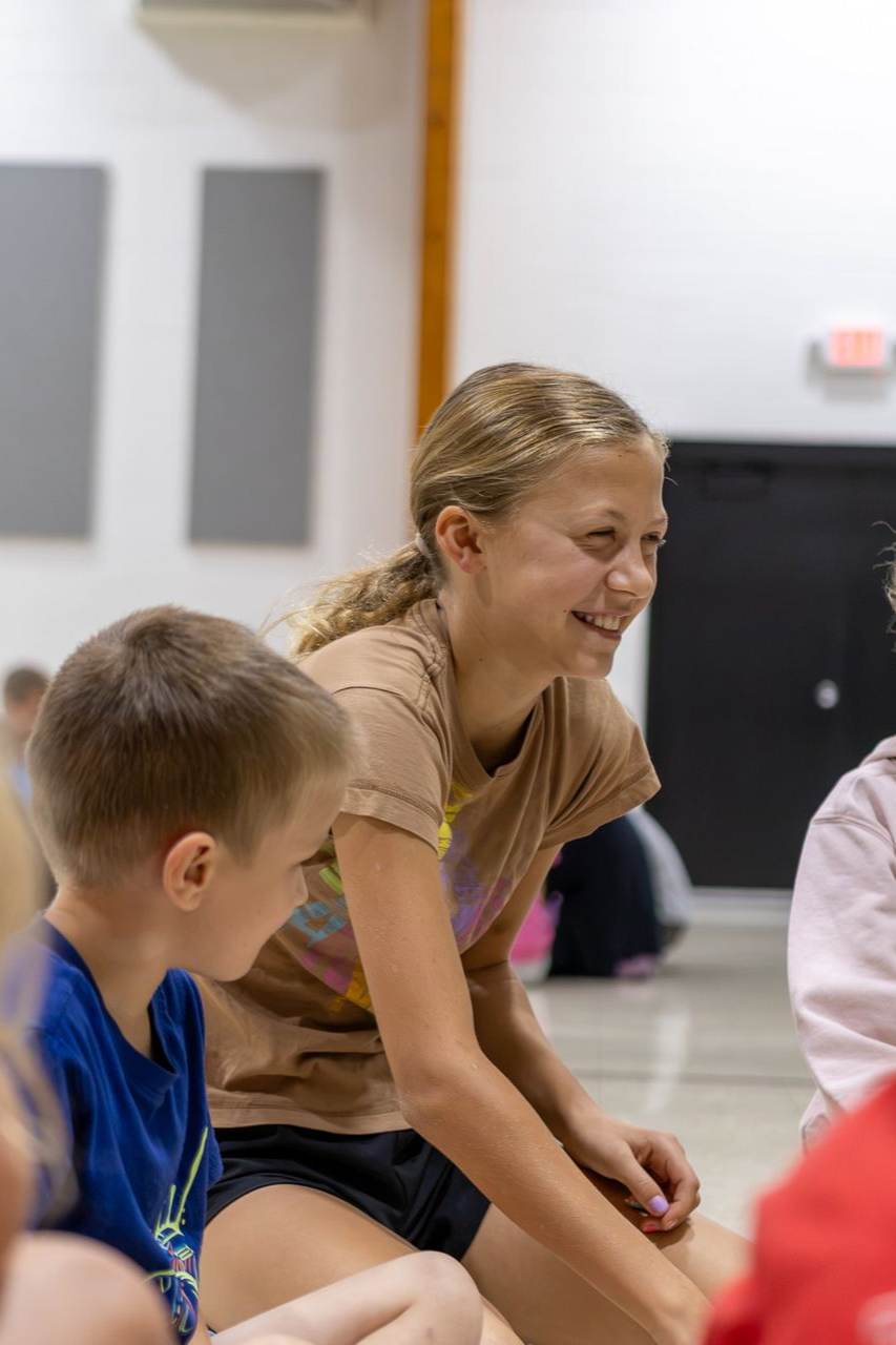 Smiling older student sitting with a younger student during a gym activity