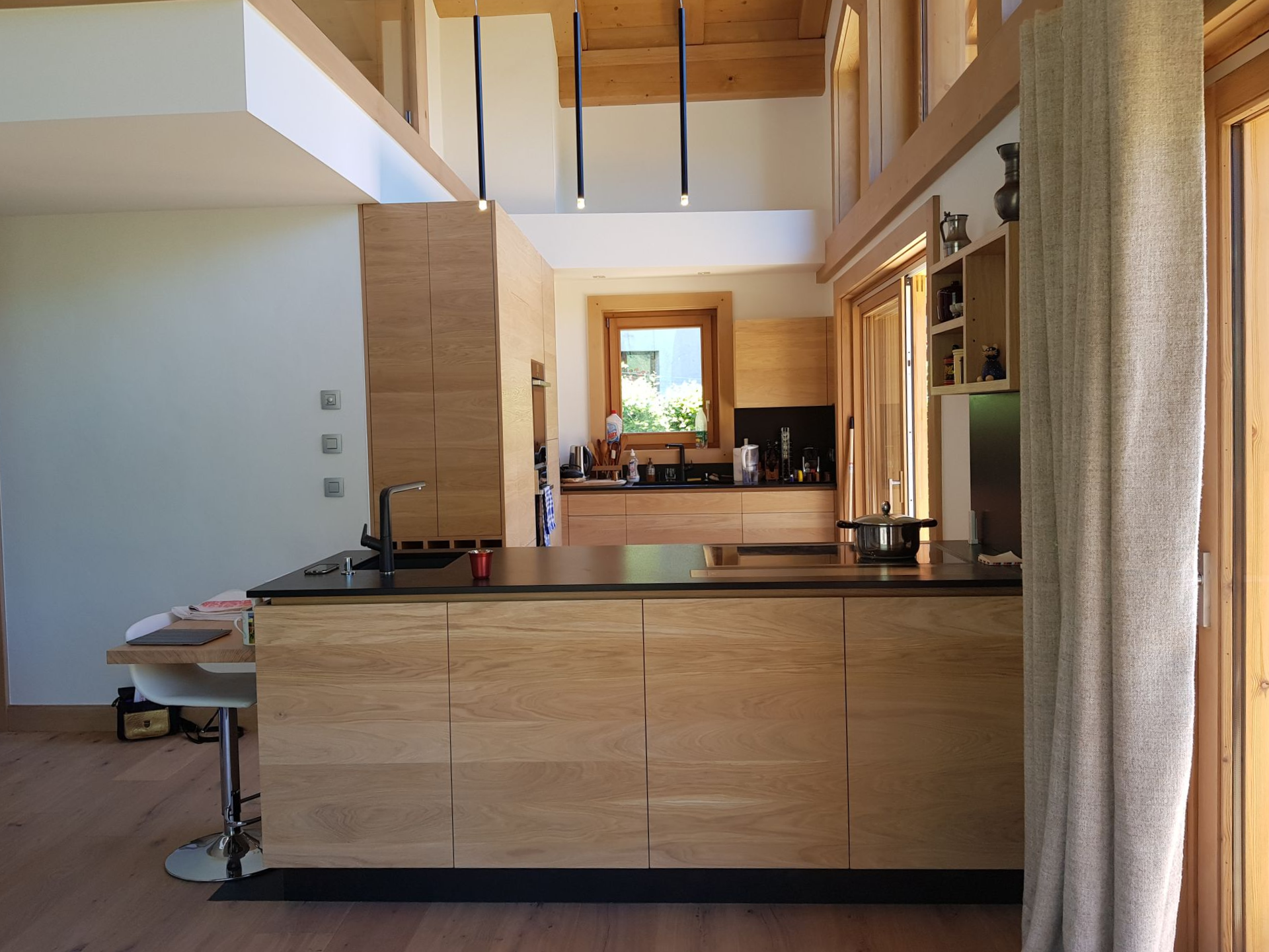 Cuisine moderne avec placards en bois clair, îlot central et grandes fenêtres.