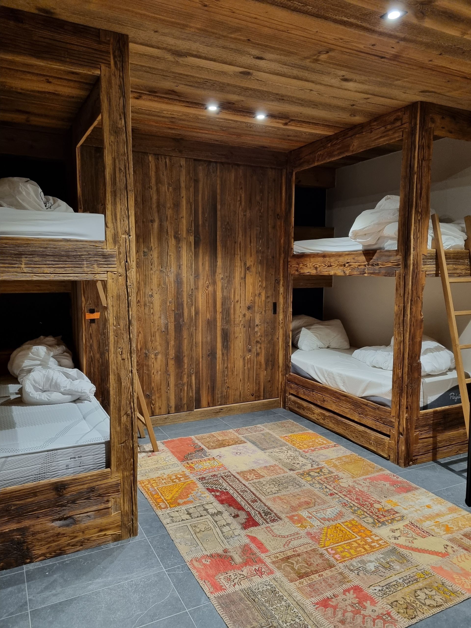 Lits superposés rustiques dans une chambre en bois avec un tapis à motifs colorés.