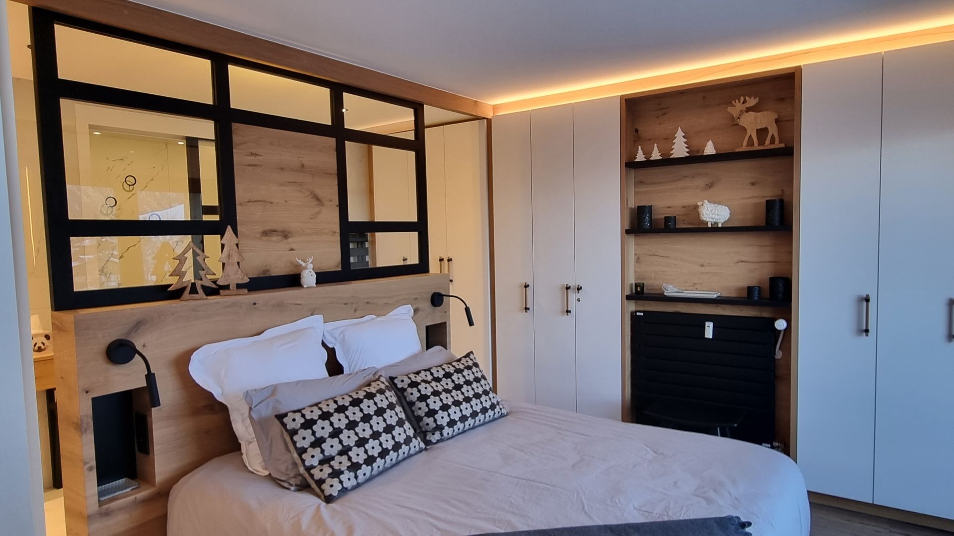 Chambre confortable avec un lit, des éléments en bois, un miroir à cadre noir et un placard intégré.