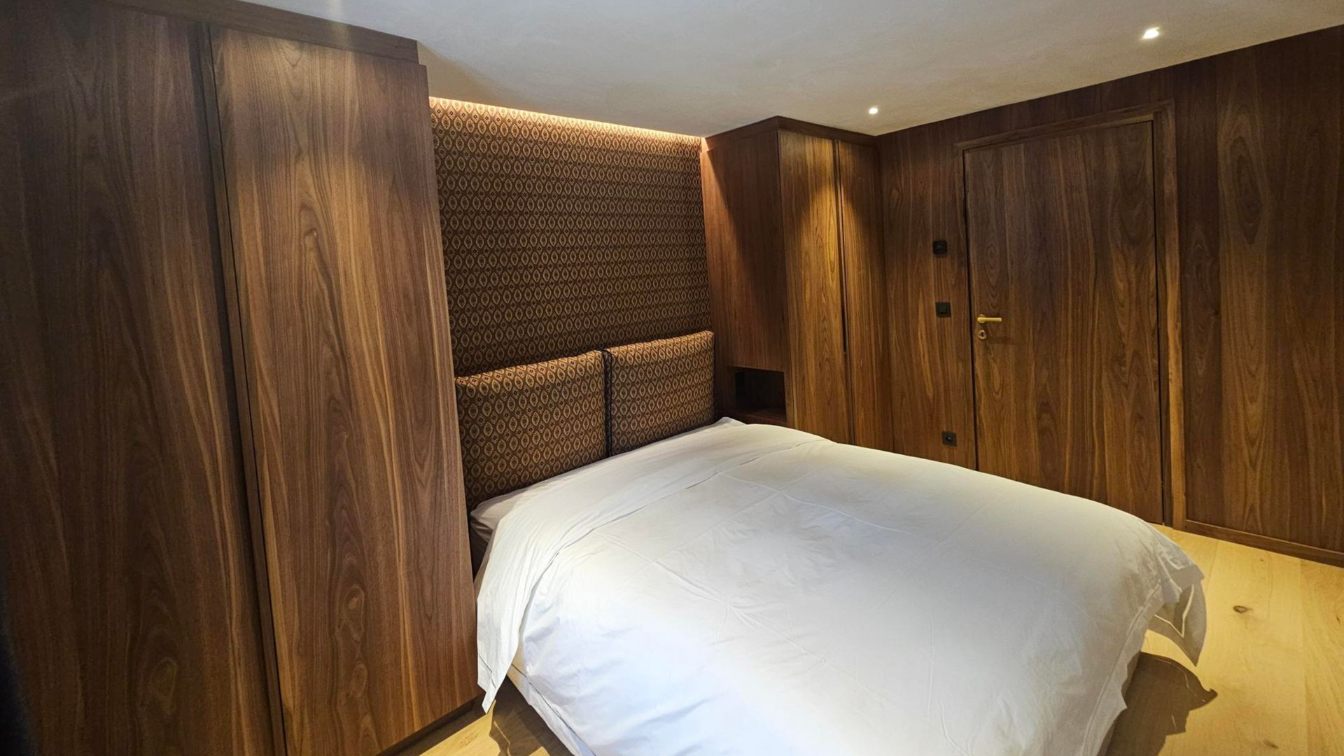 Chambre avec lambris, un lit avec linge de lit blanc et des armoires encastrées.